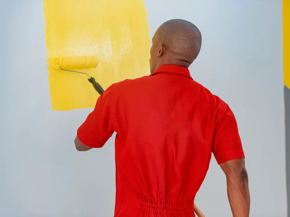 Pintor a aplicar tinta amarela com rolo